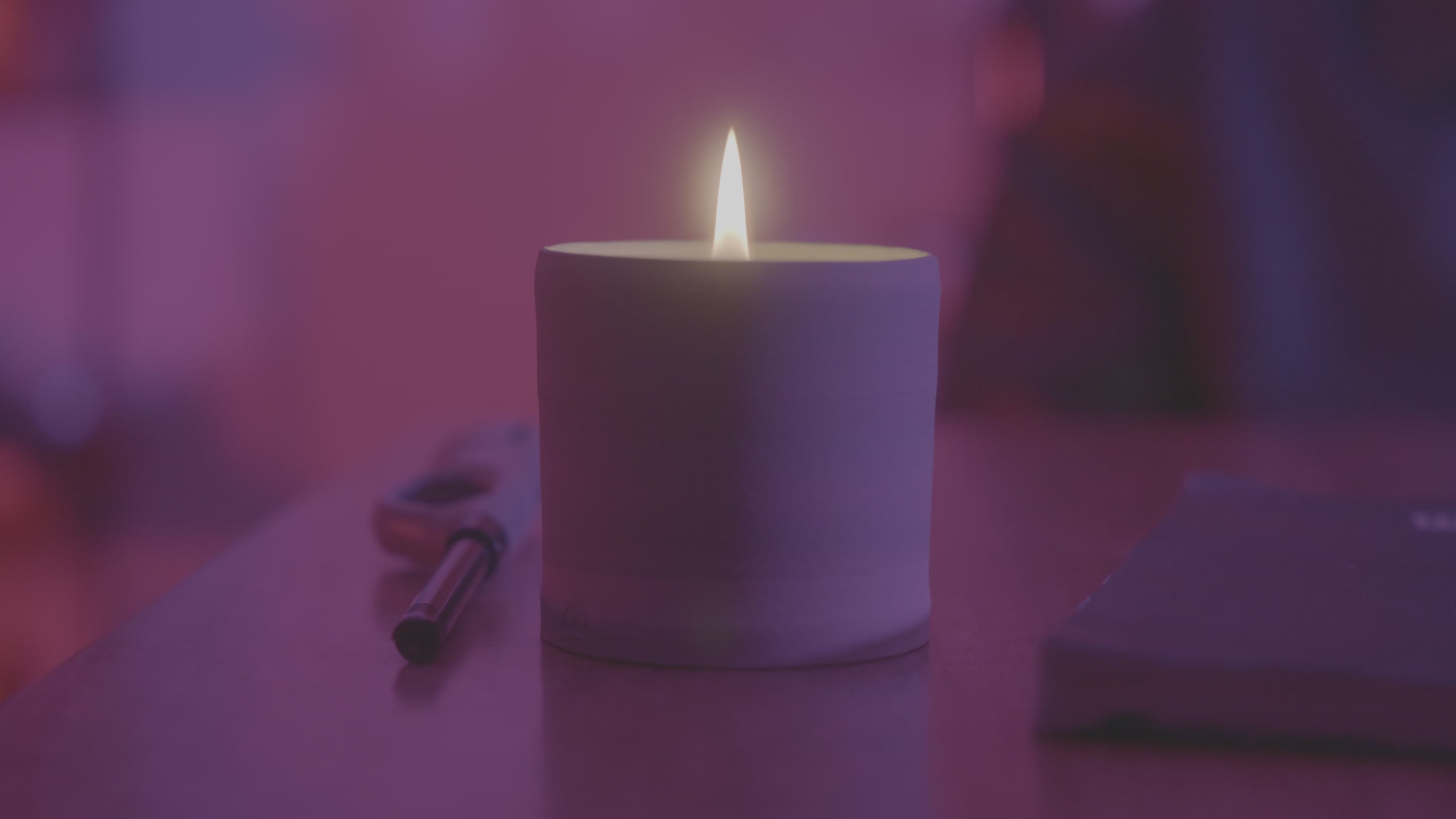 Lit Thirdwall candle glowing in a dark room with soft purple lighting and a lighter nearby.